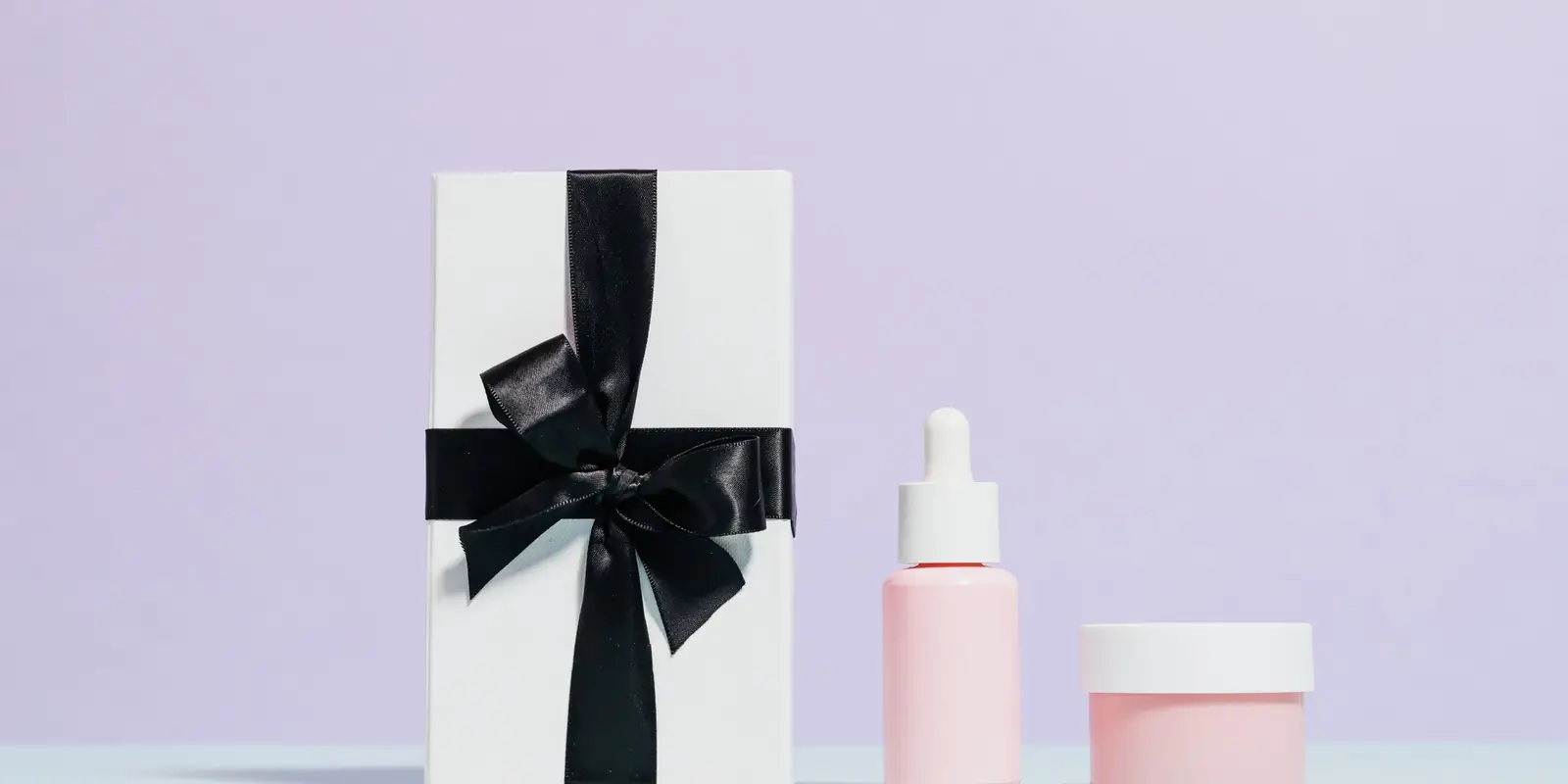 Unbranded skincare bottle and jar beside a white gift box tied with black ribbon