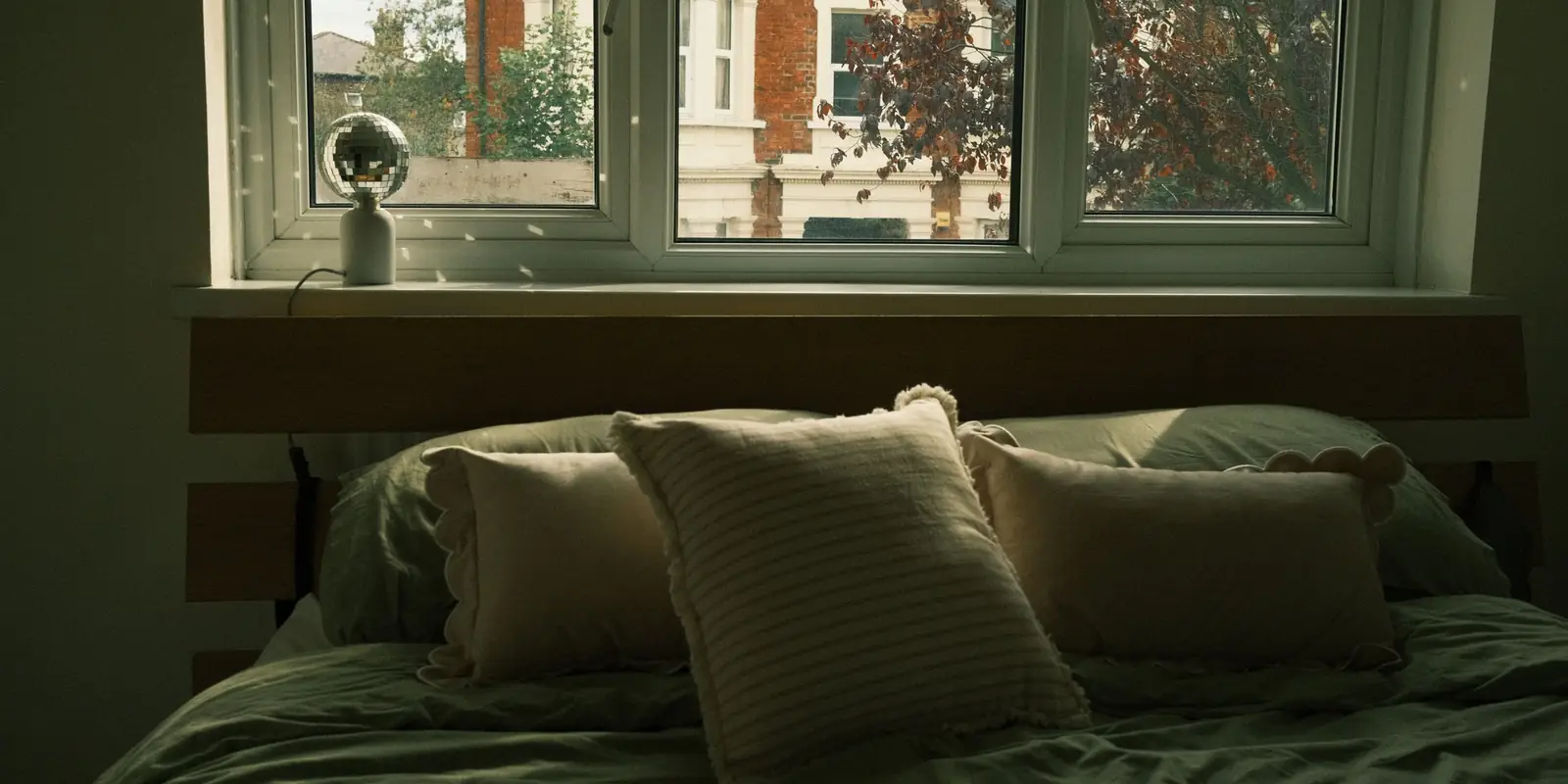 A bed with soft pillows beside a large window in autumn light