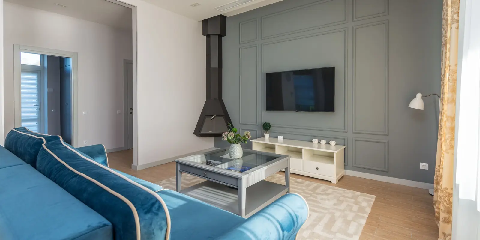Living room with a blue sofa, coffee table and a wall-mounted TV on a grey panelled wall