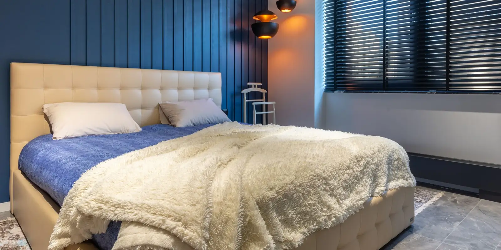 Made double bed with a cream blanket and pillows beside warm bedside lamps