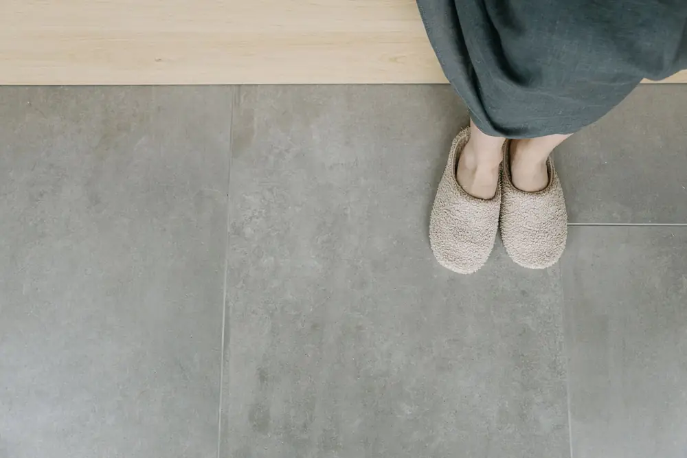 Feet in grey slippers on a cold tiled floor