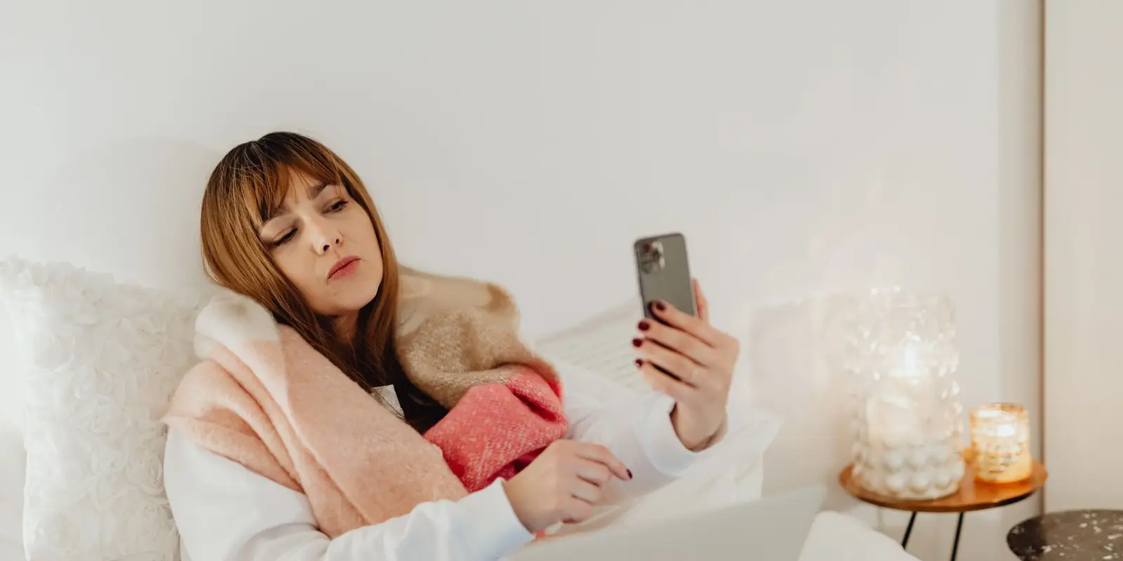 Woman wrapped in a scarf on a sofa using her phone and laptop