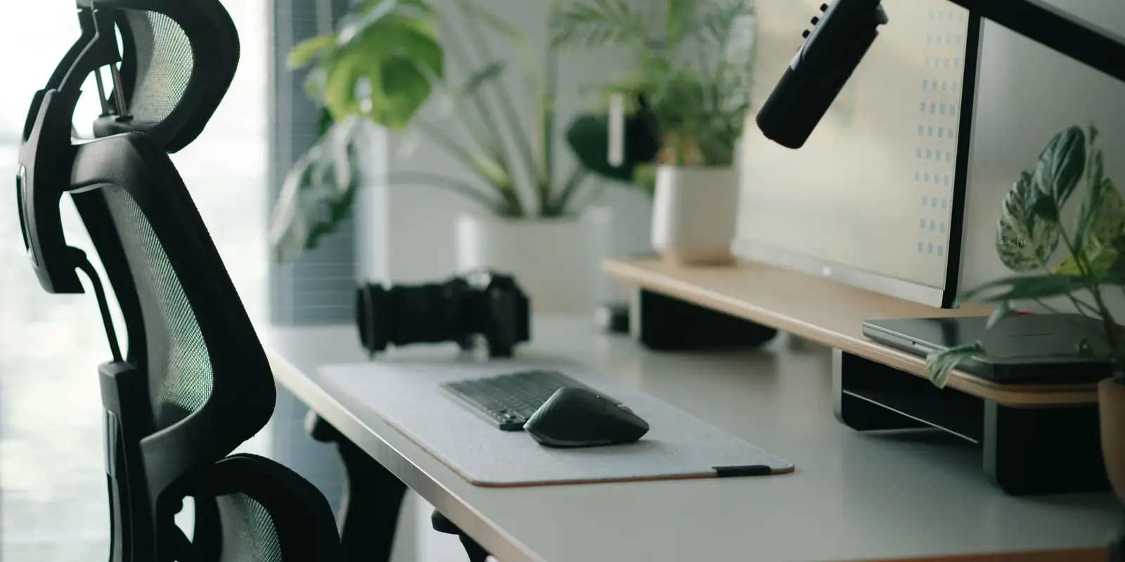 Black mesh ergonomic chair with a headrest at a white home-office desk with plants