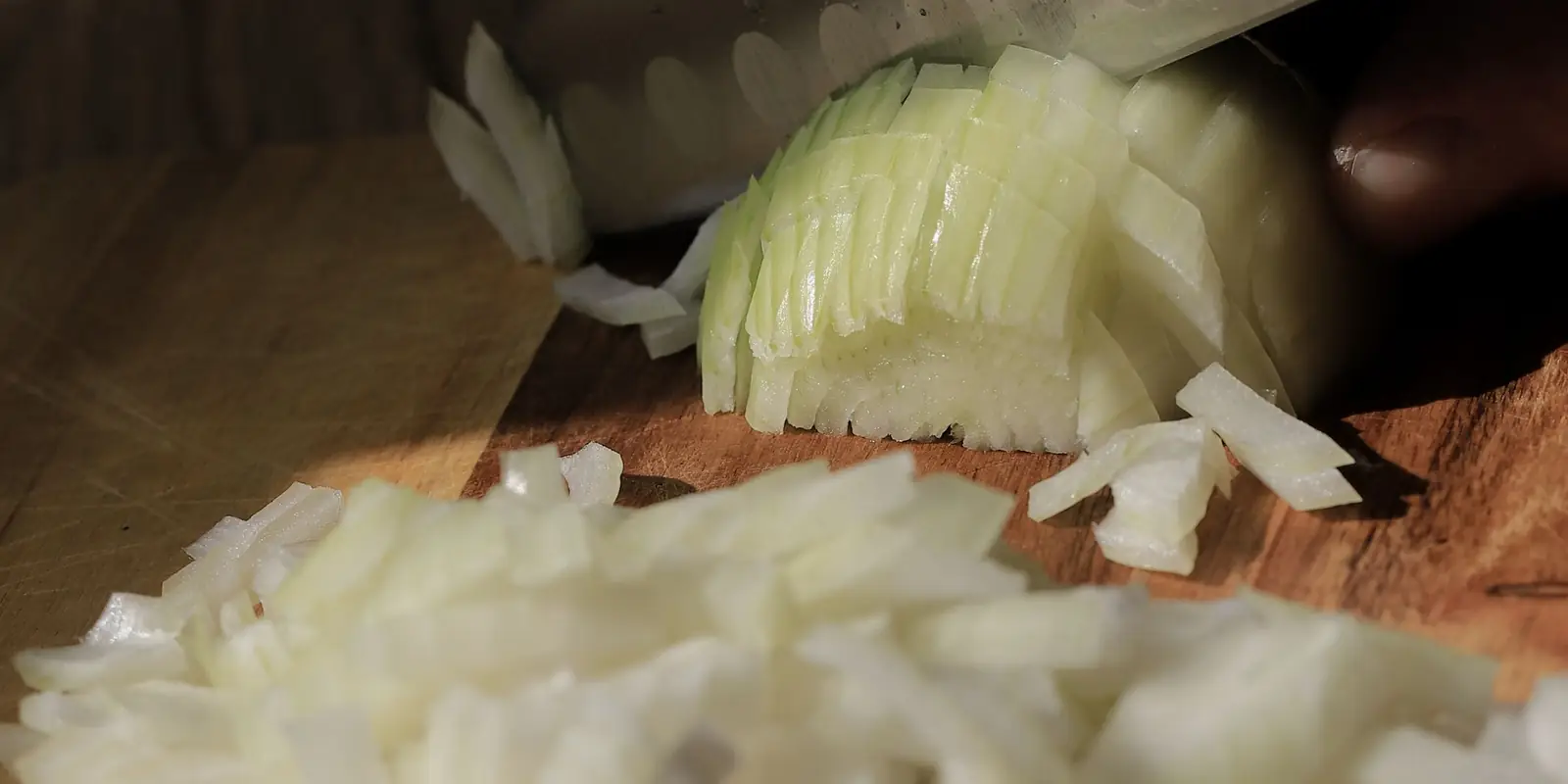 Onion being finely chopped on a wooden board