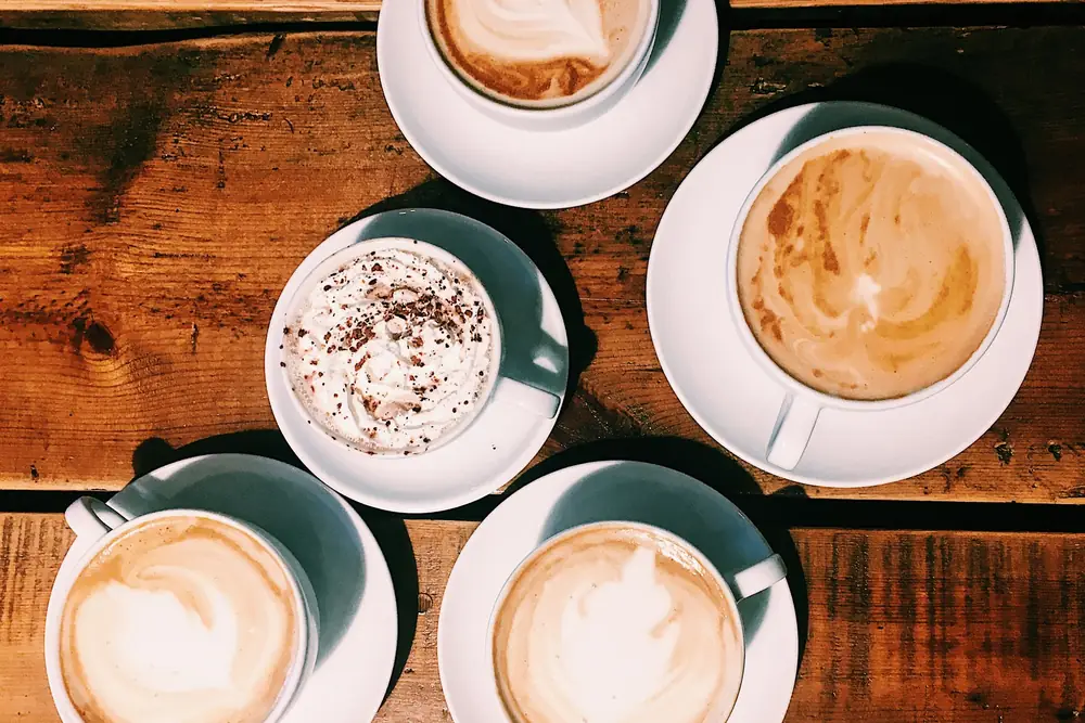 Four milky coffees with latte art on a wooden table