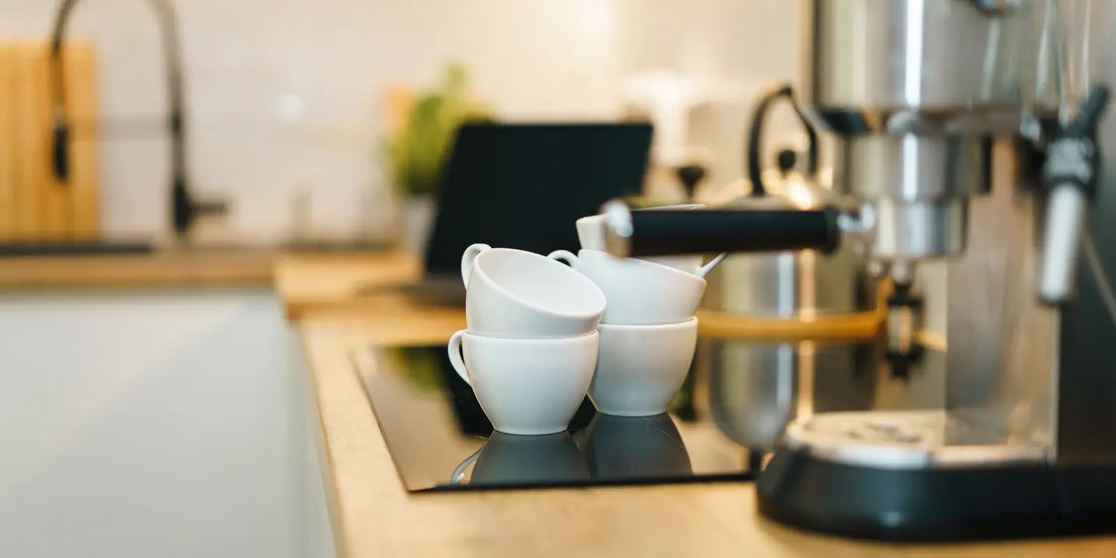 Espresso machine on a kitchen worktop with white cups stacked on top