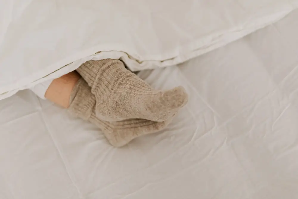 Feet in thick knitted socks peeking out from under a white duvet