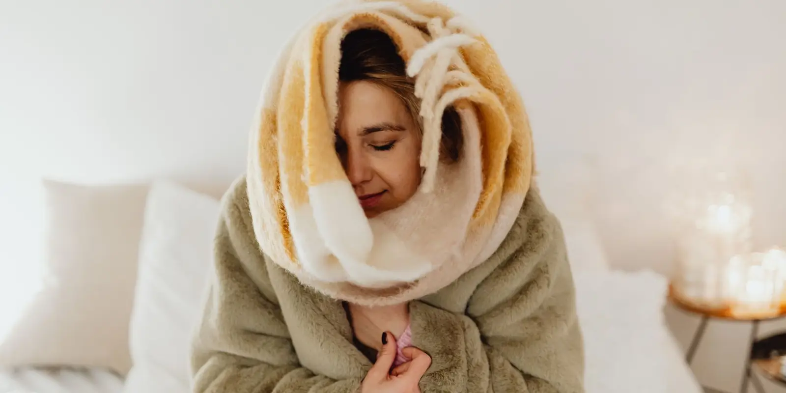 Woman wrapped in a fluffy blanket sitting on a bed