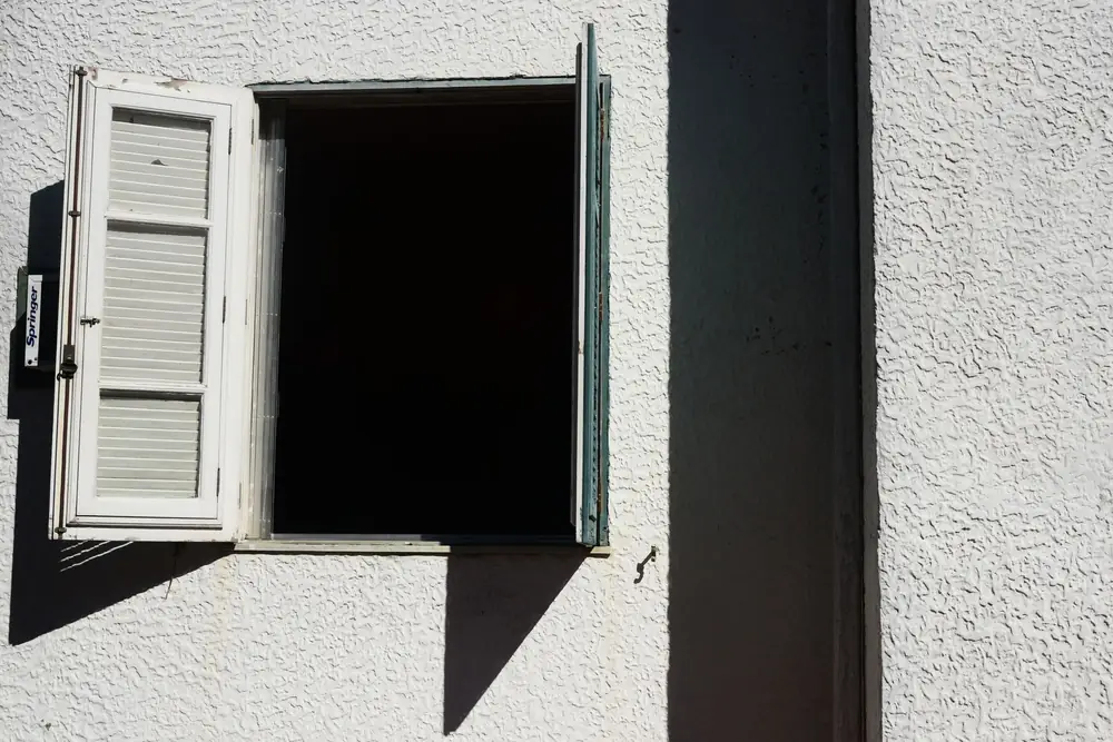 Window with a white frame opened outwards in a pale rendered wall