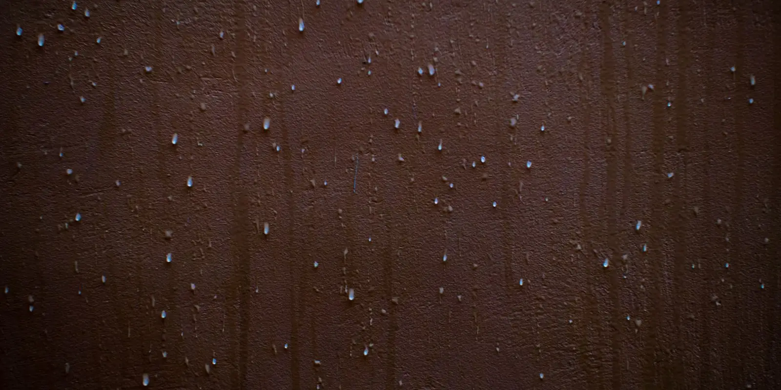 Small beads of water on a dark brown wall