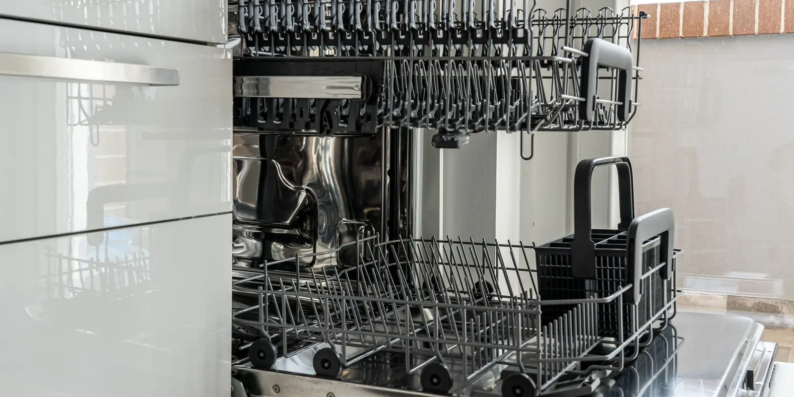 Open dishwasher with empty racks and cutlery basket in a white gloss kitchen