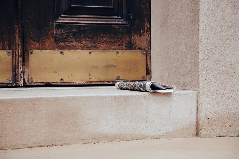 Folded newspaper on a stone step at the foot of an old wooden door