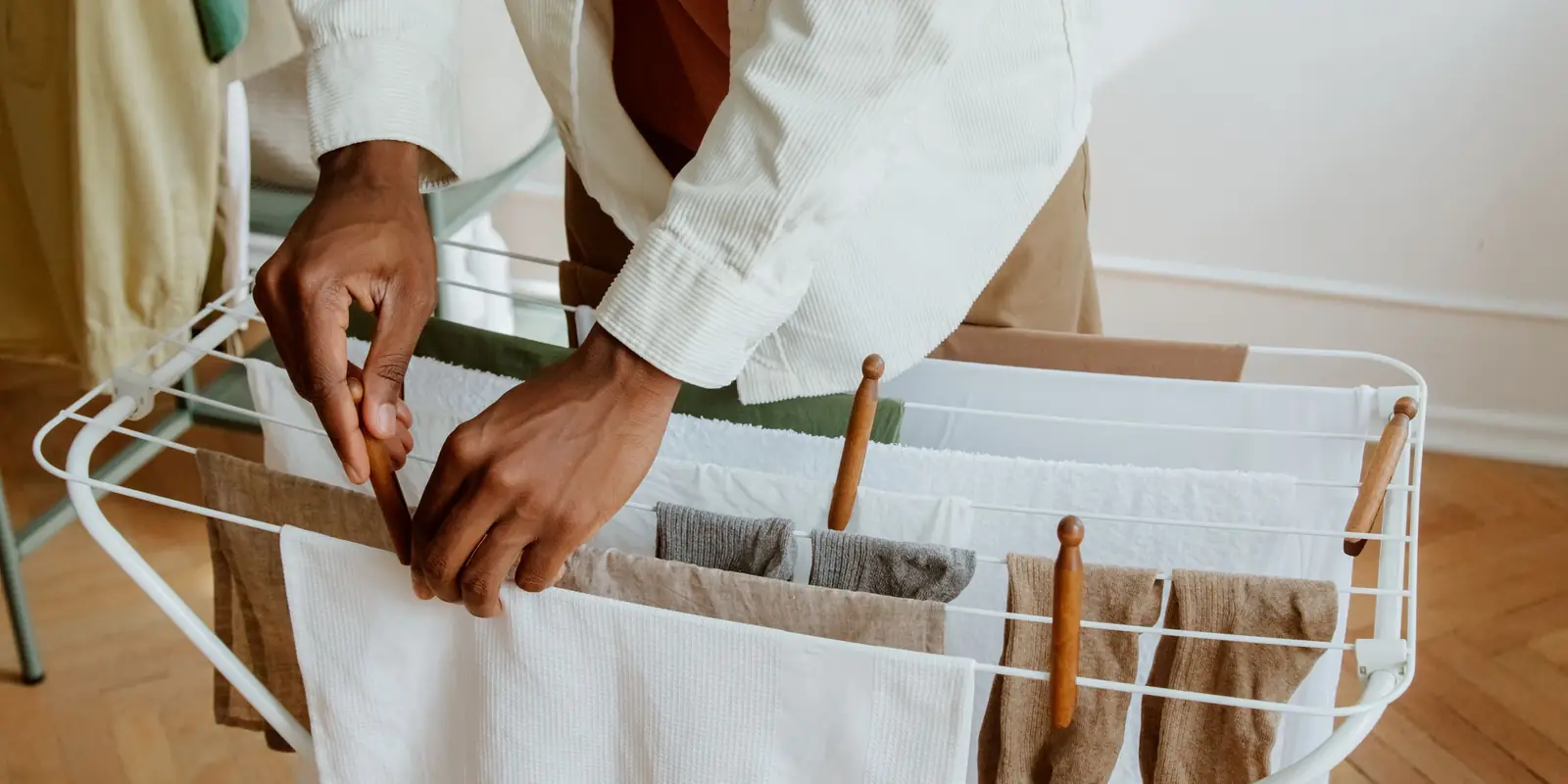 A person hanging clean washing on an indoor drying rack