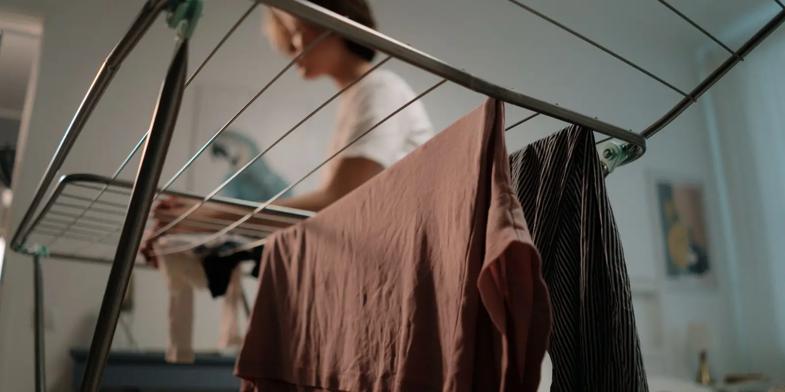 Person hanging washing on a metal clothes airer indoors