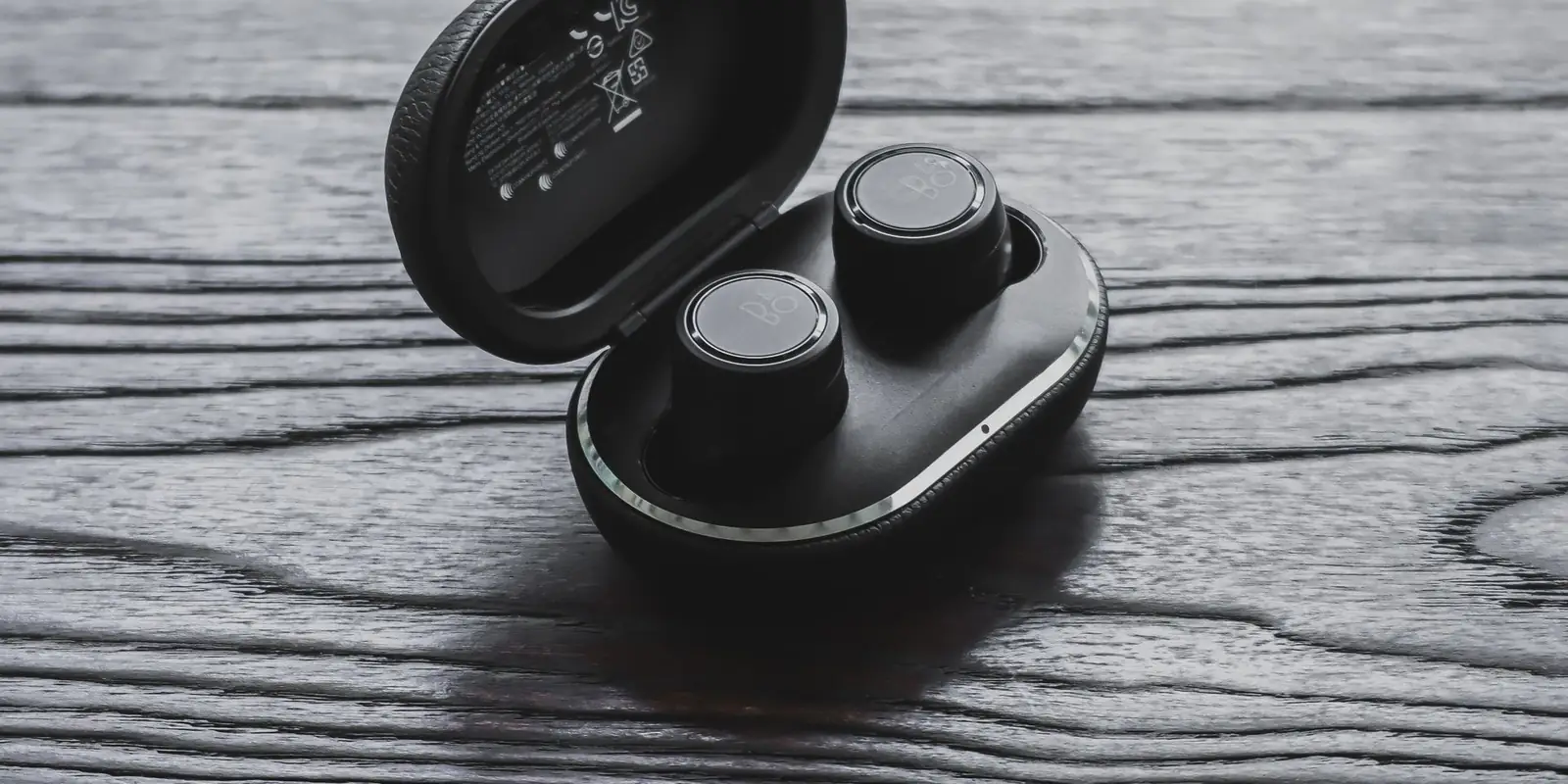 Black wireless earbuds and their charging case on a grey wooden surface
