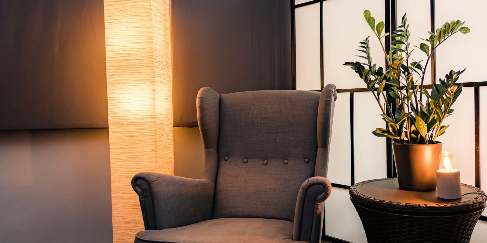 An armchair beside a glowing floor lamp and a candle in a warm, dimly lit room