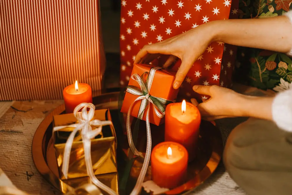 Hands placing a small wrapped present beside lit candles and other gifts