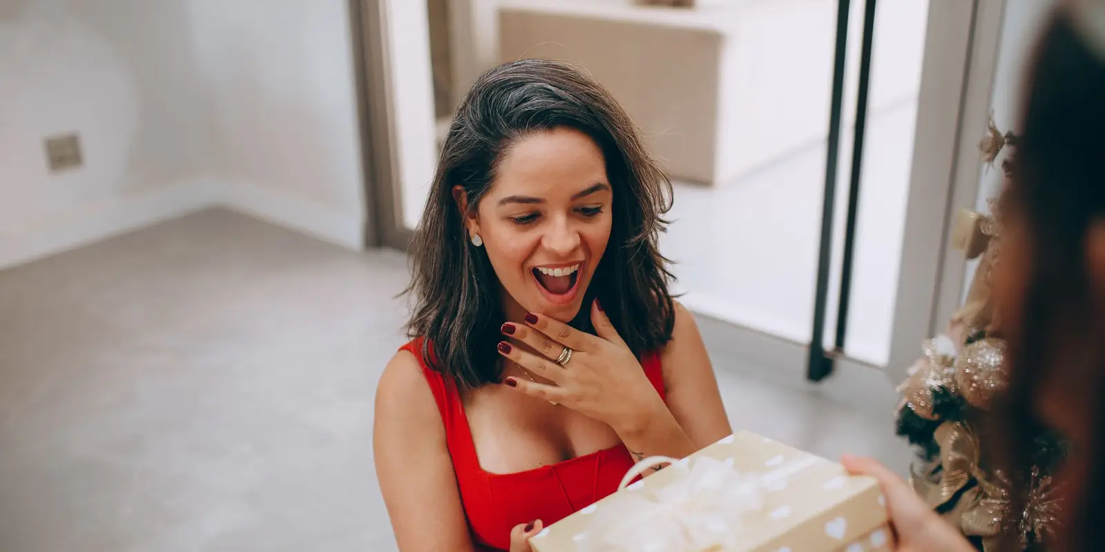 Delighted woman in a red dress being handed a wrapped Christmas present