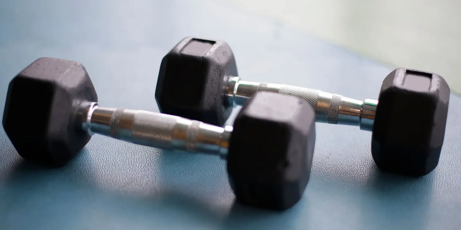 Pair of black hex dumbbells with chrome handles on a blue floor