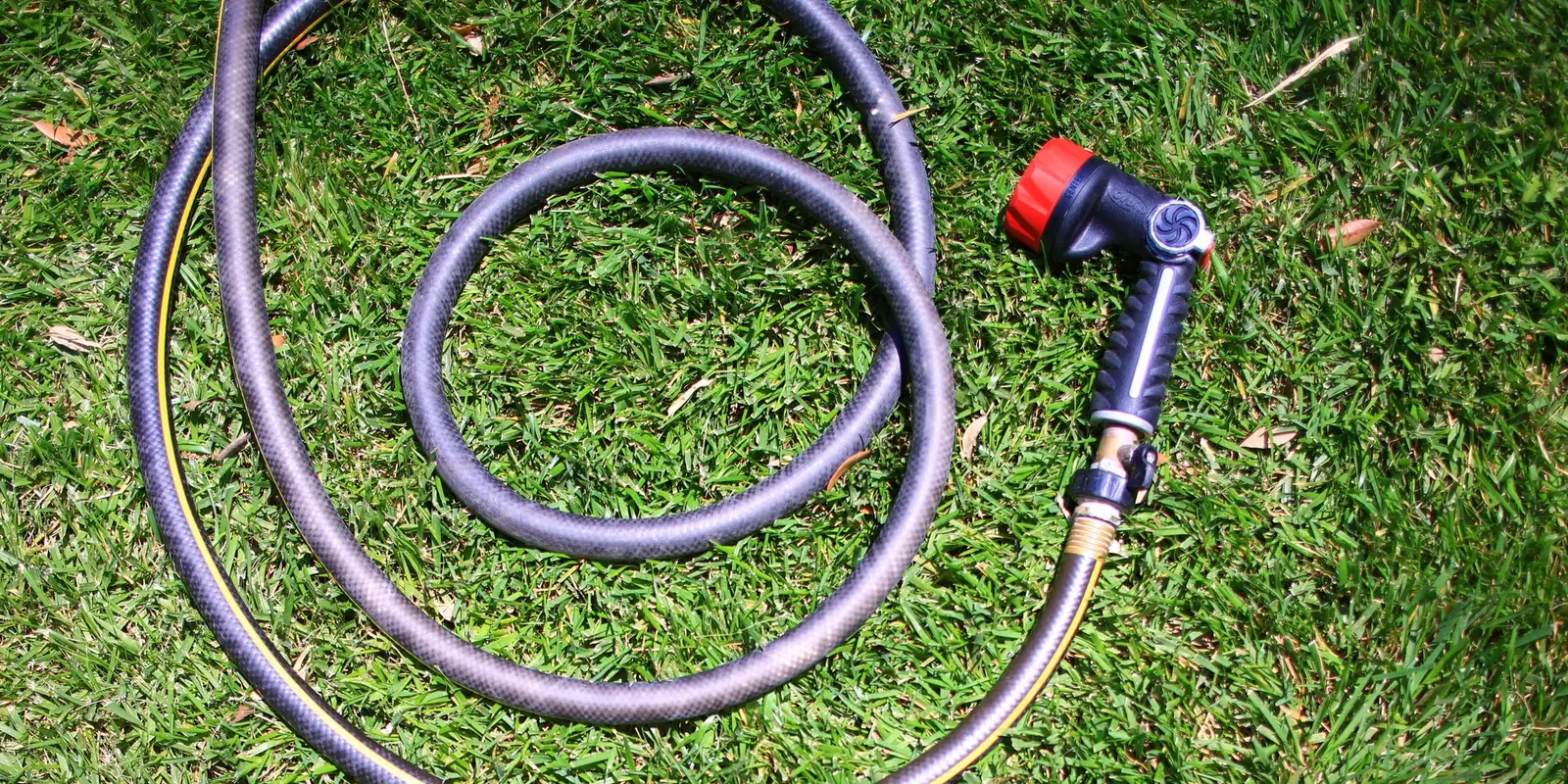 Coiled garden hose with a spray nozzle lying on a green lawn