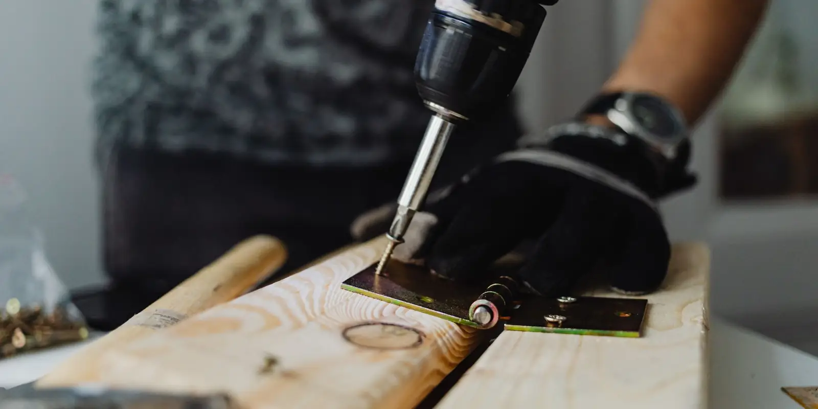 A hand driving a screw into wood with a cordless drill