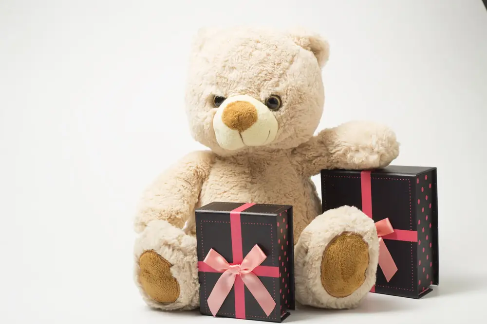 Cream teddy bear sitting between two black gift boxes tied with pink ribbon