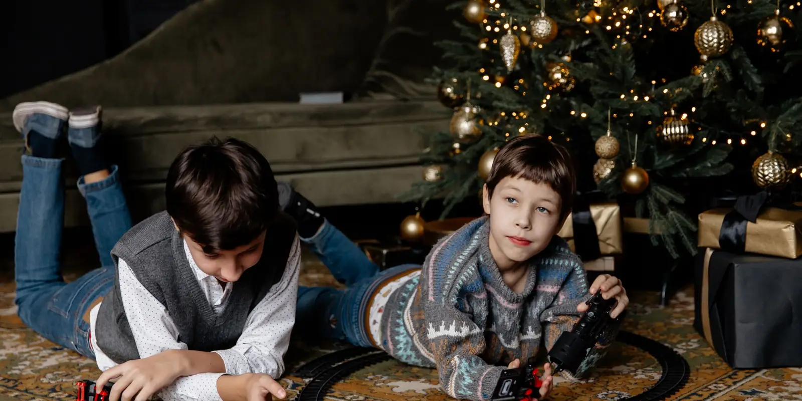 Two young boys playing with a toy train set by a Christmas tree