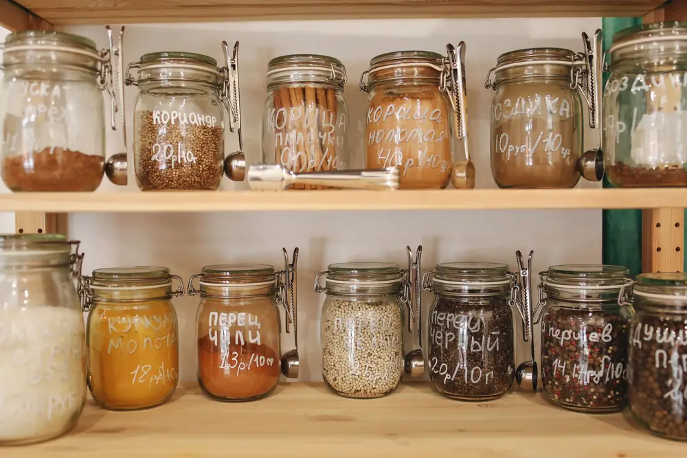 Rows of glass storage jars filled with dry ingredients on wooden shelves