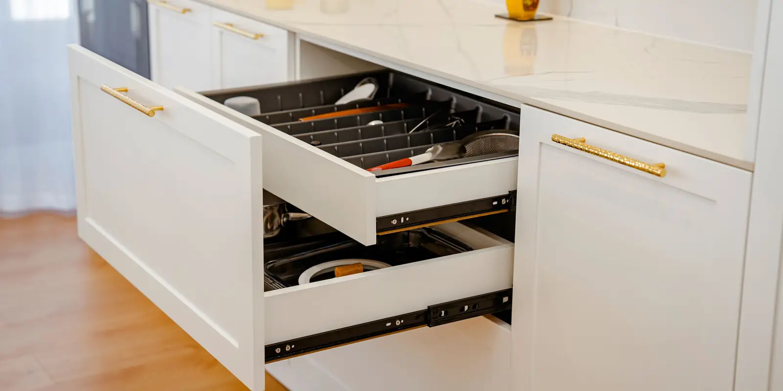 White kitchen with an open drawer of neatly organised utensils below a marble worktop