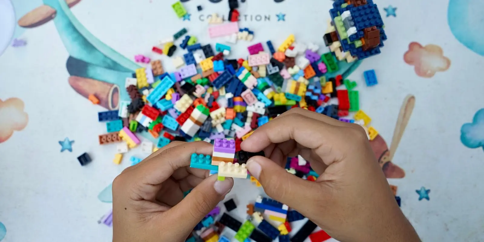 Hands of a child building with colourful LEGO bricks on an outdoor table