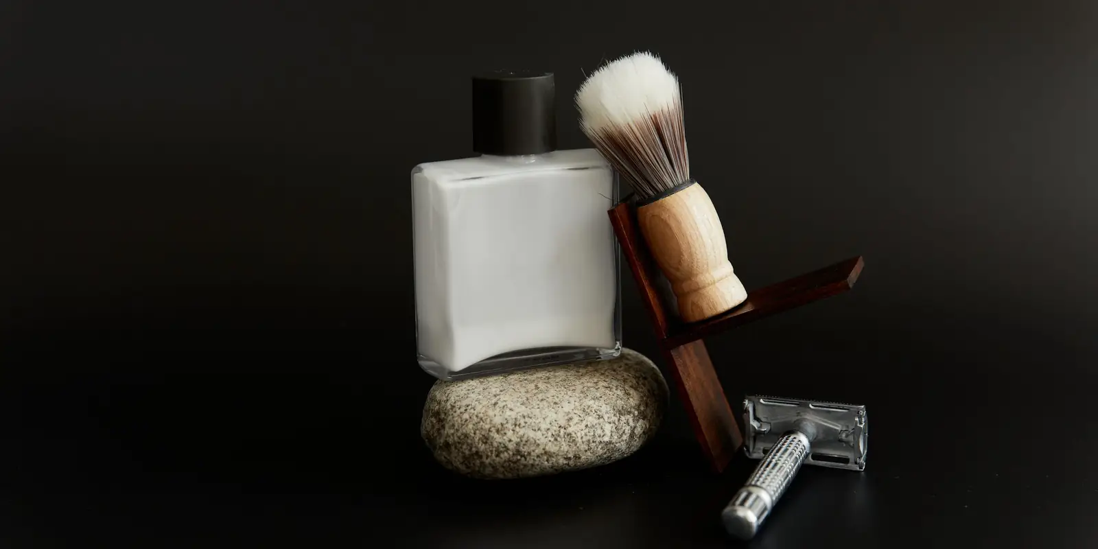 Shaving brush, razor and a plain white bottle on a dark background
