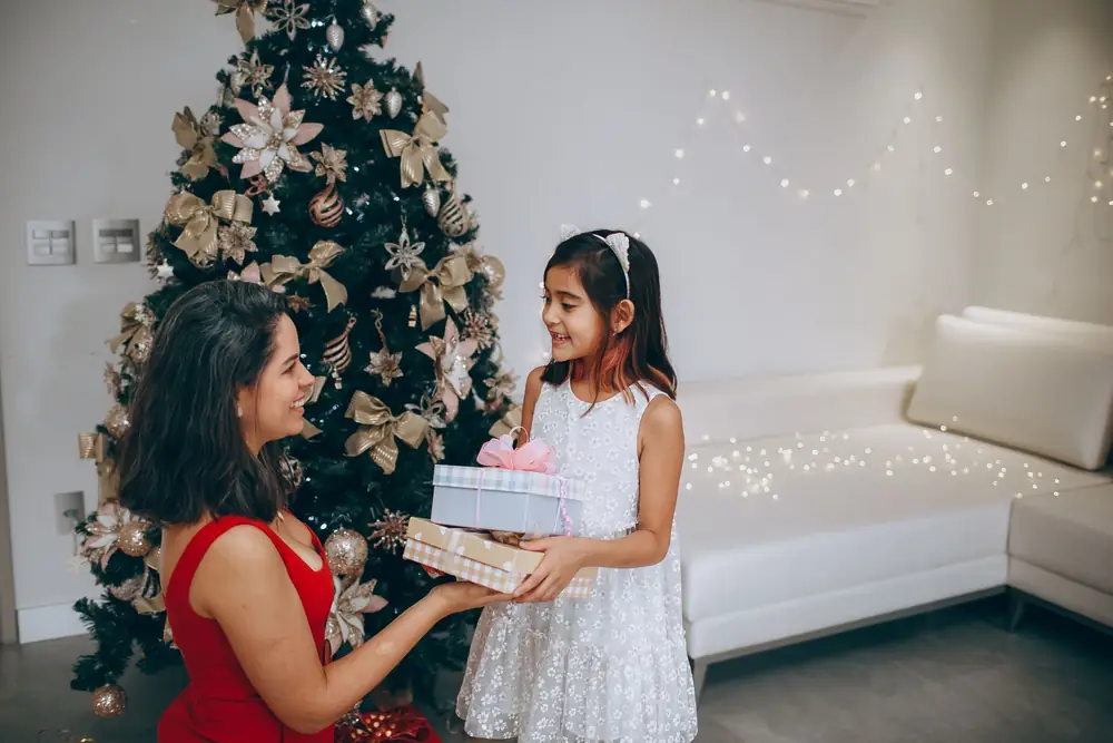 Mother and daughter exchanging a wrapped present beside a Christmas tree