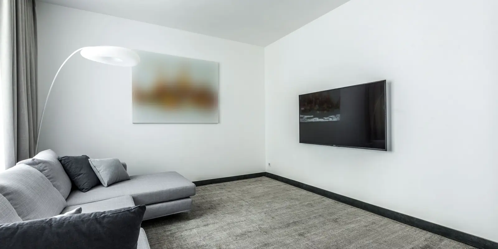 Minimal living room with a grey corner sofa, arc floor lamp and a slim TV mounted on a white wall