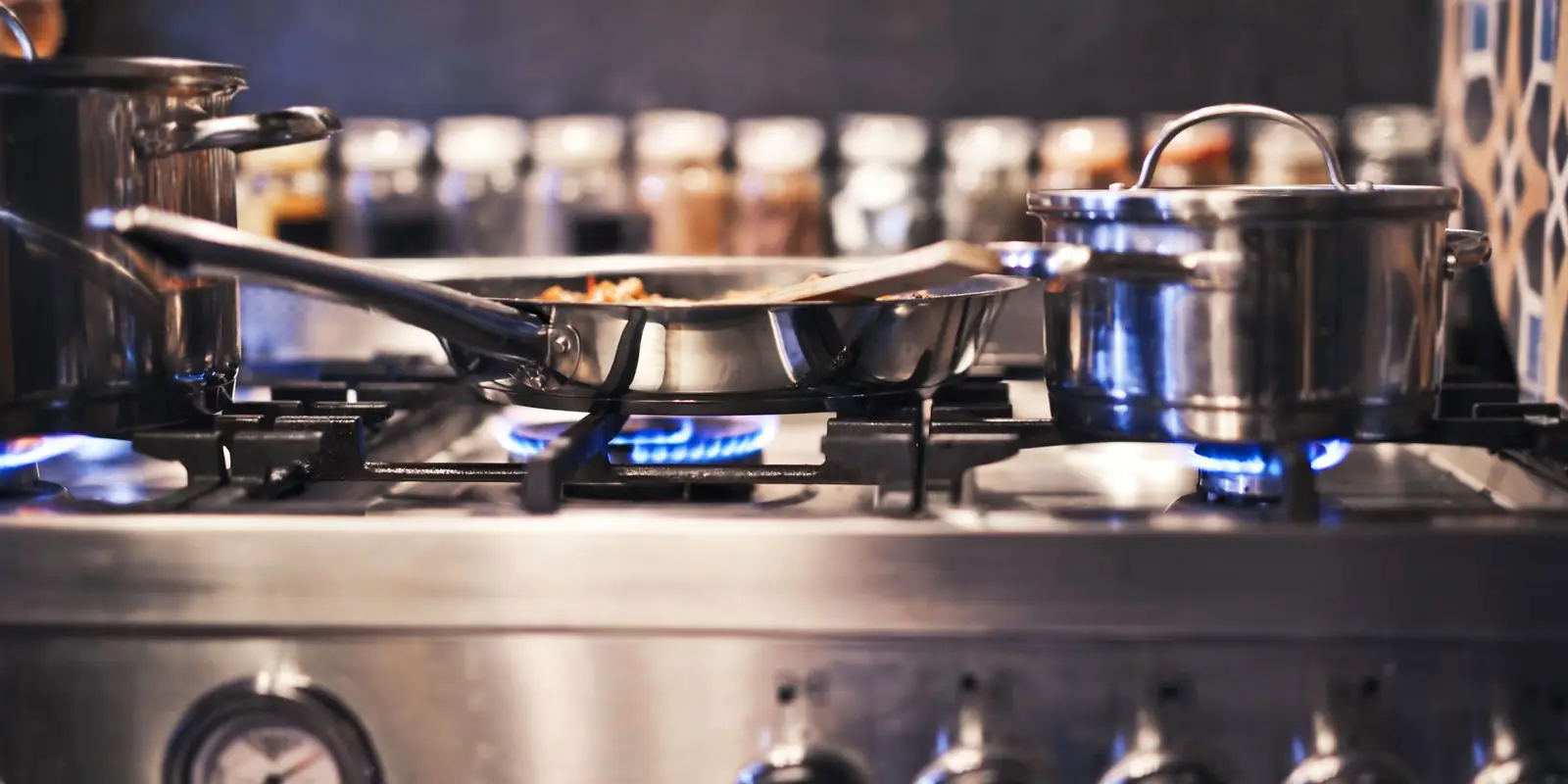 Stainless steel pots and pans on a gas hob with blue flames