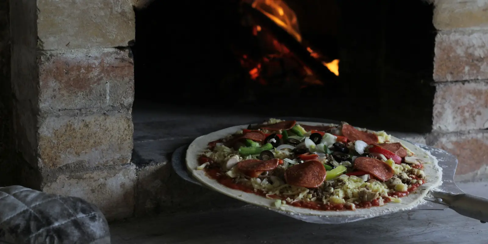 A pizza cooking at the mouth of a brick oven with flames inside