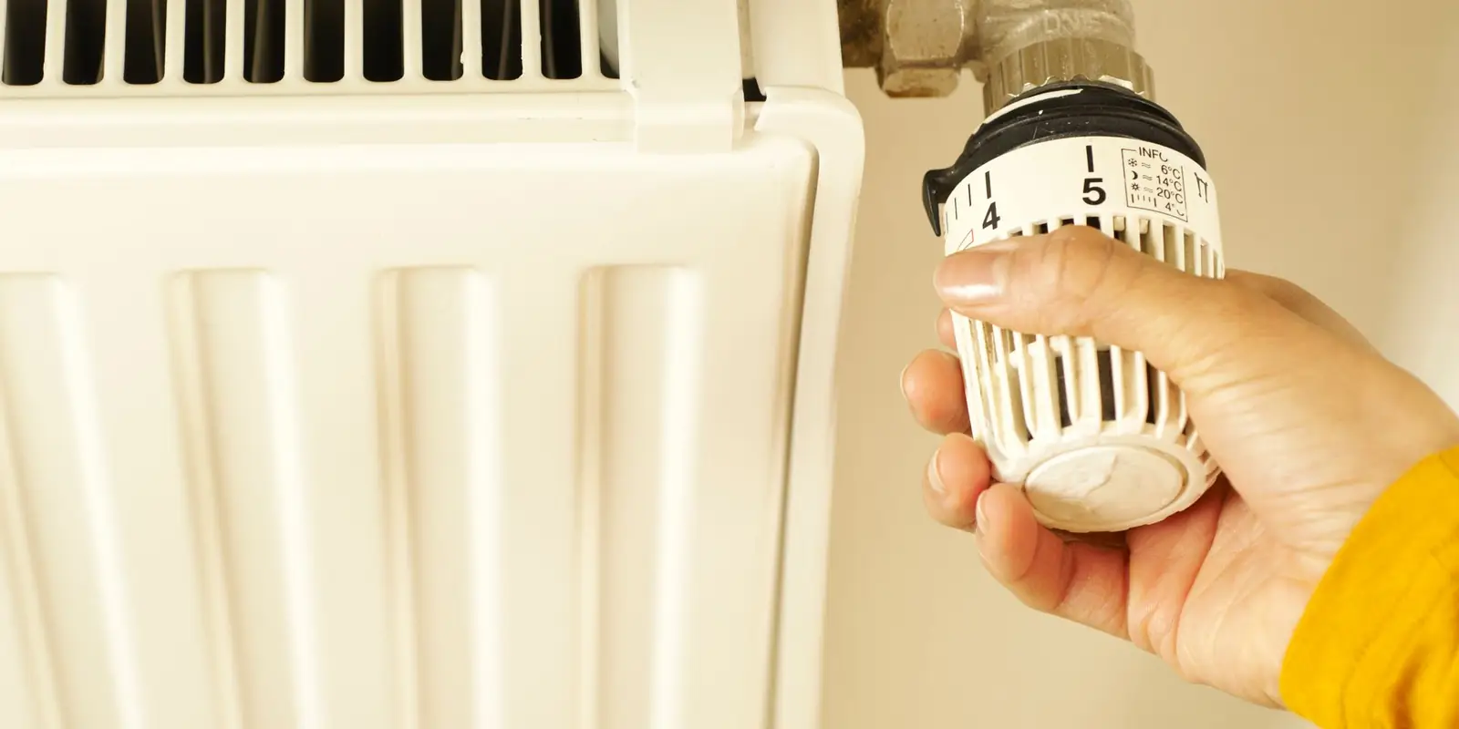 Hand turning the thermostatic valve on a white radiator