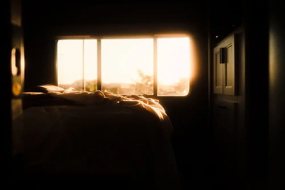 Warm sunrise light glowing through a small window into a dark bedroom