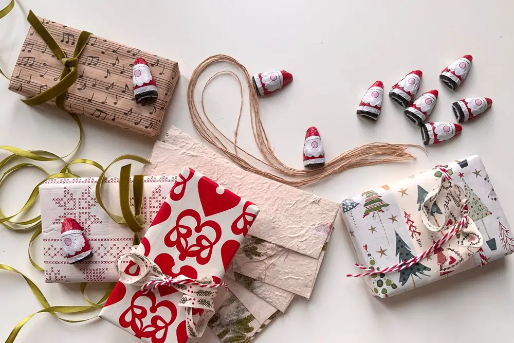 Wrapped Christmas presents, twine and small chocolate Santas on a white table