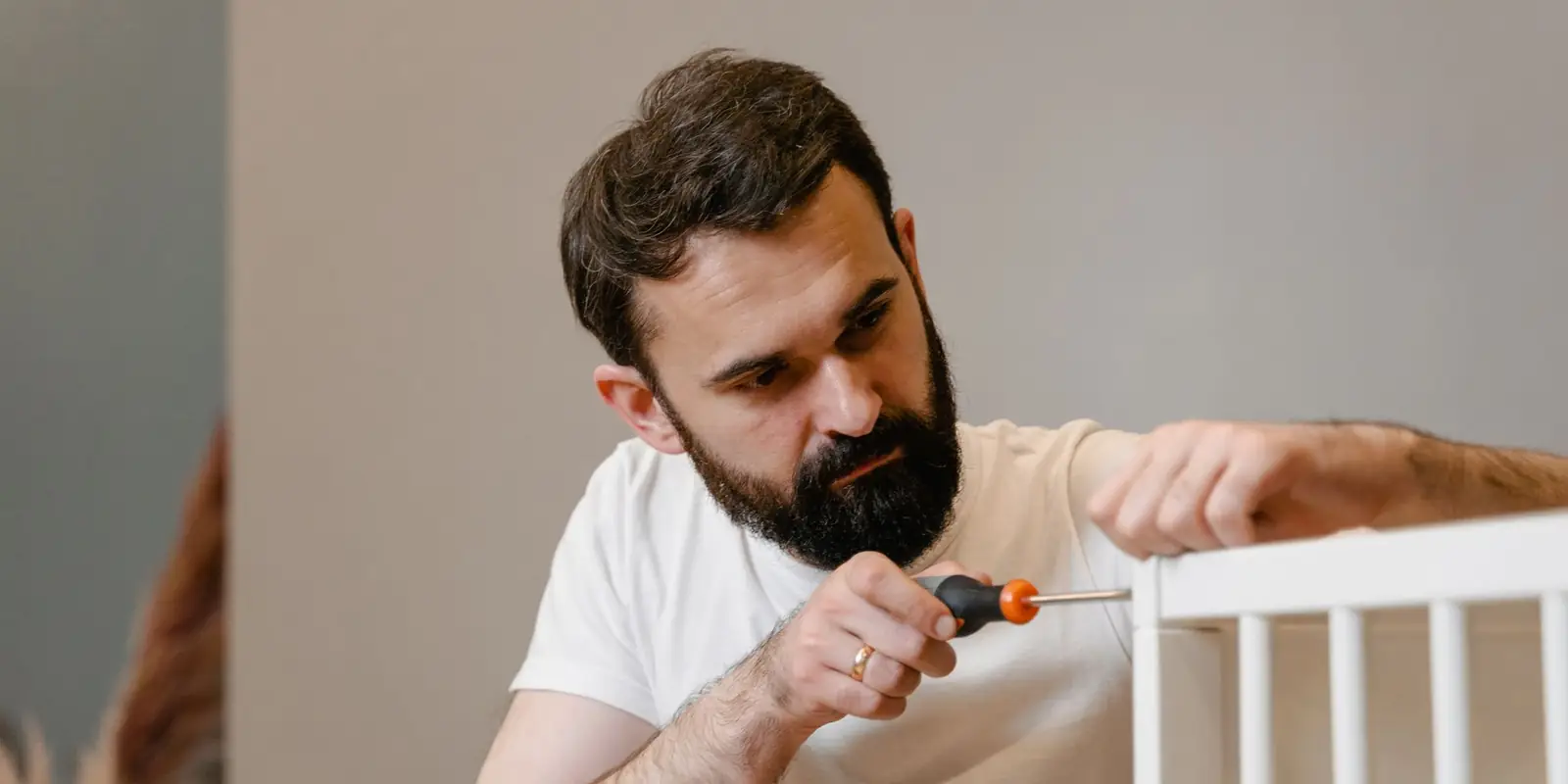Man using a screwdriver to assemble a white wooden cot