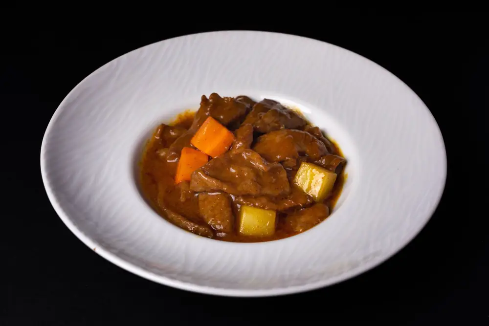 Bowl of beef stew with carrots and potatoes on a dark table