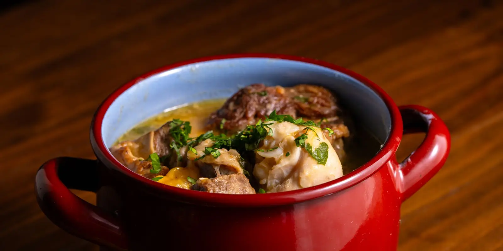 Hearty meat and vegetable stew in a red pot on a wooden table