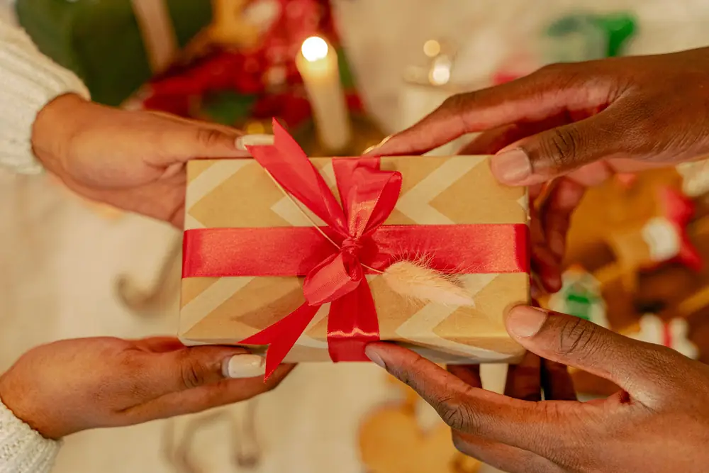 Two hands passing a small present wrapped with a red ribbon