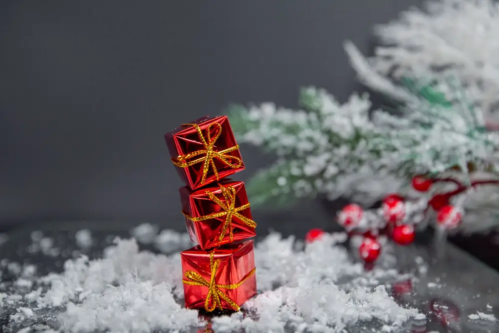 Stack of small red gift boxes with gold ribbon beside a snowy spruce branch