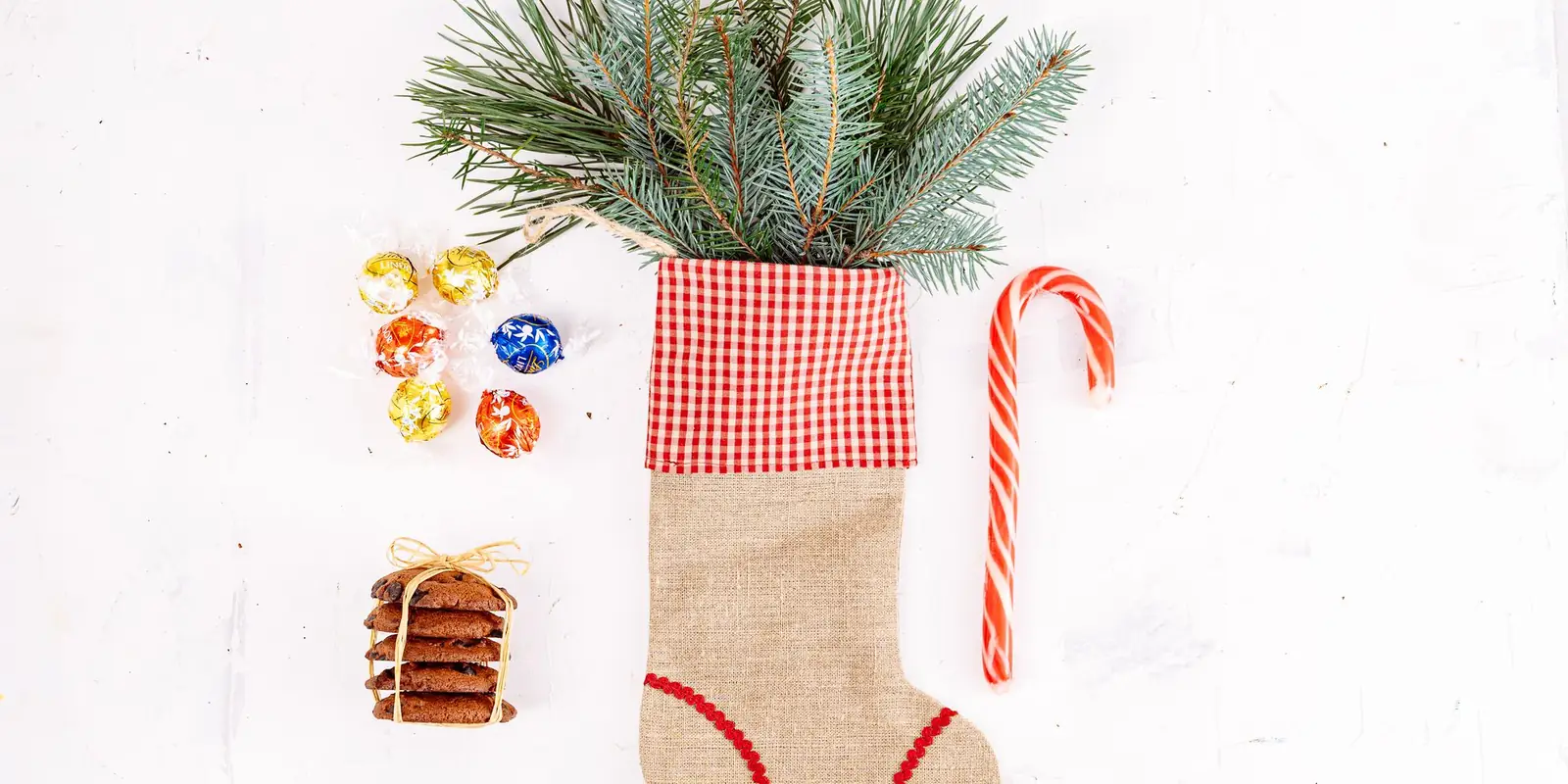 Christmas stocking filled with fir branches and a candy cane beside small treats