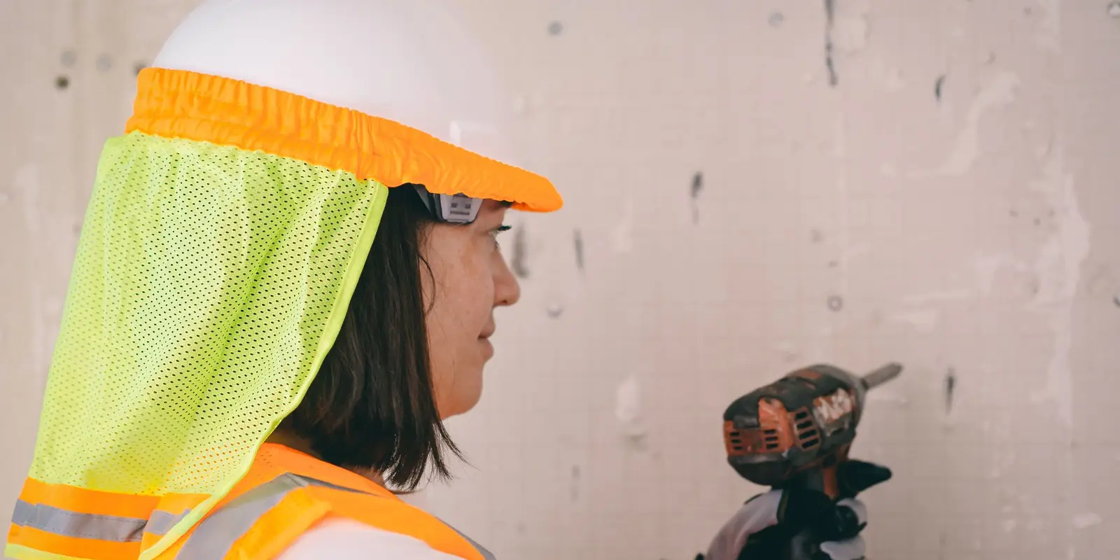 Person in a hard hat and safety glasses drilling into a plastered wall