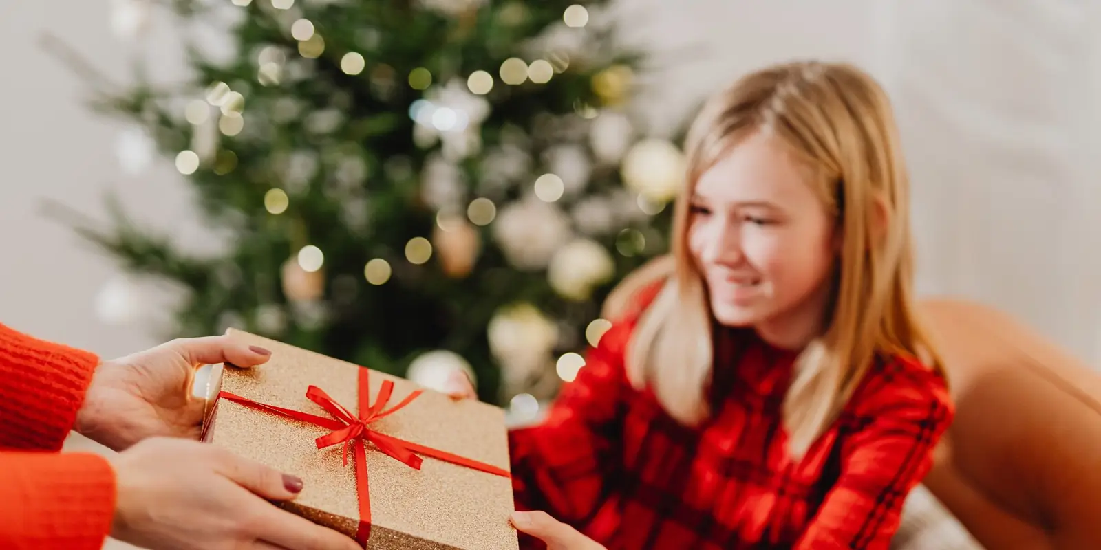 Smiling teenage girl in a red jumper receiving a wrapped Christmas present