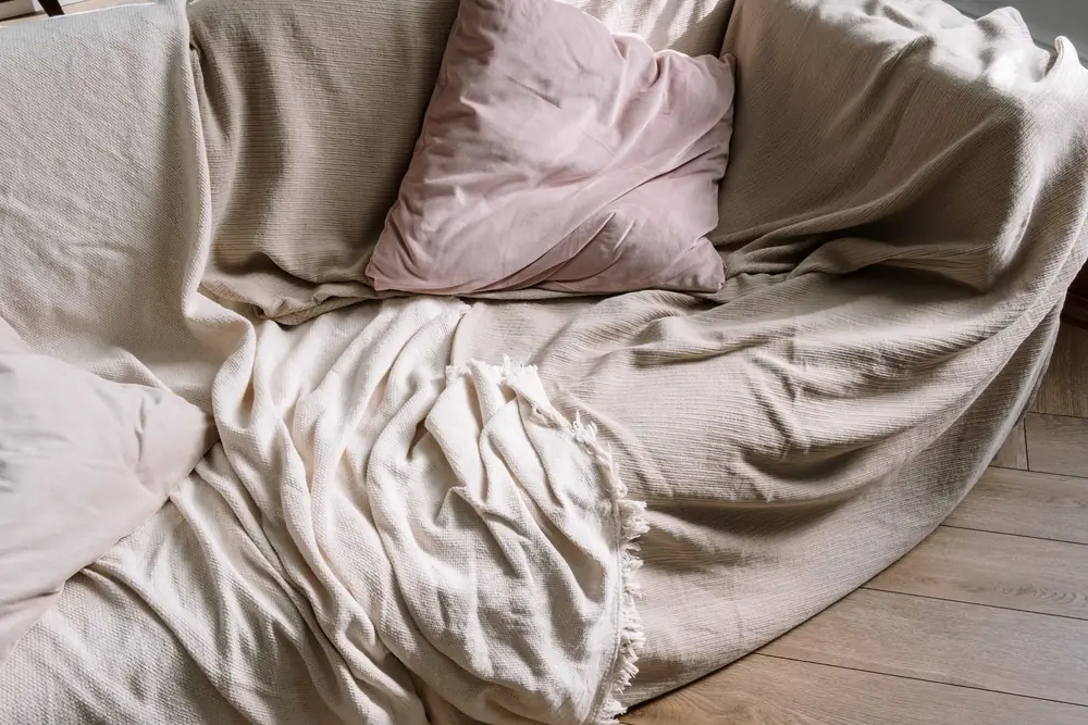Beige sofa with cushions and a soft blanket draped across it