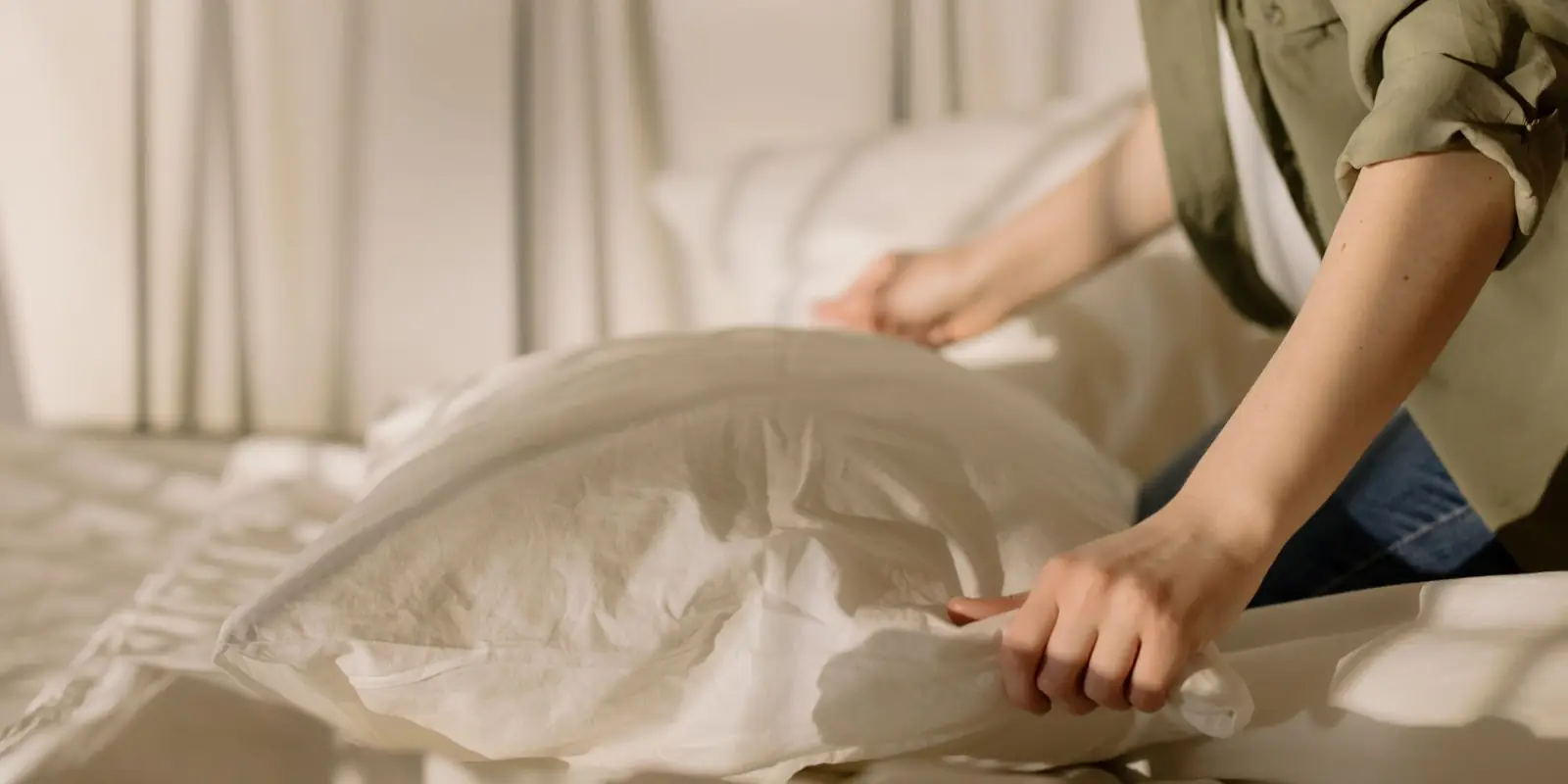 Person smoothing white bedding and pillows while making a bed