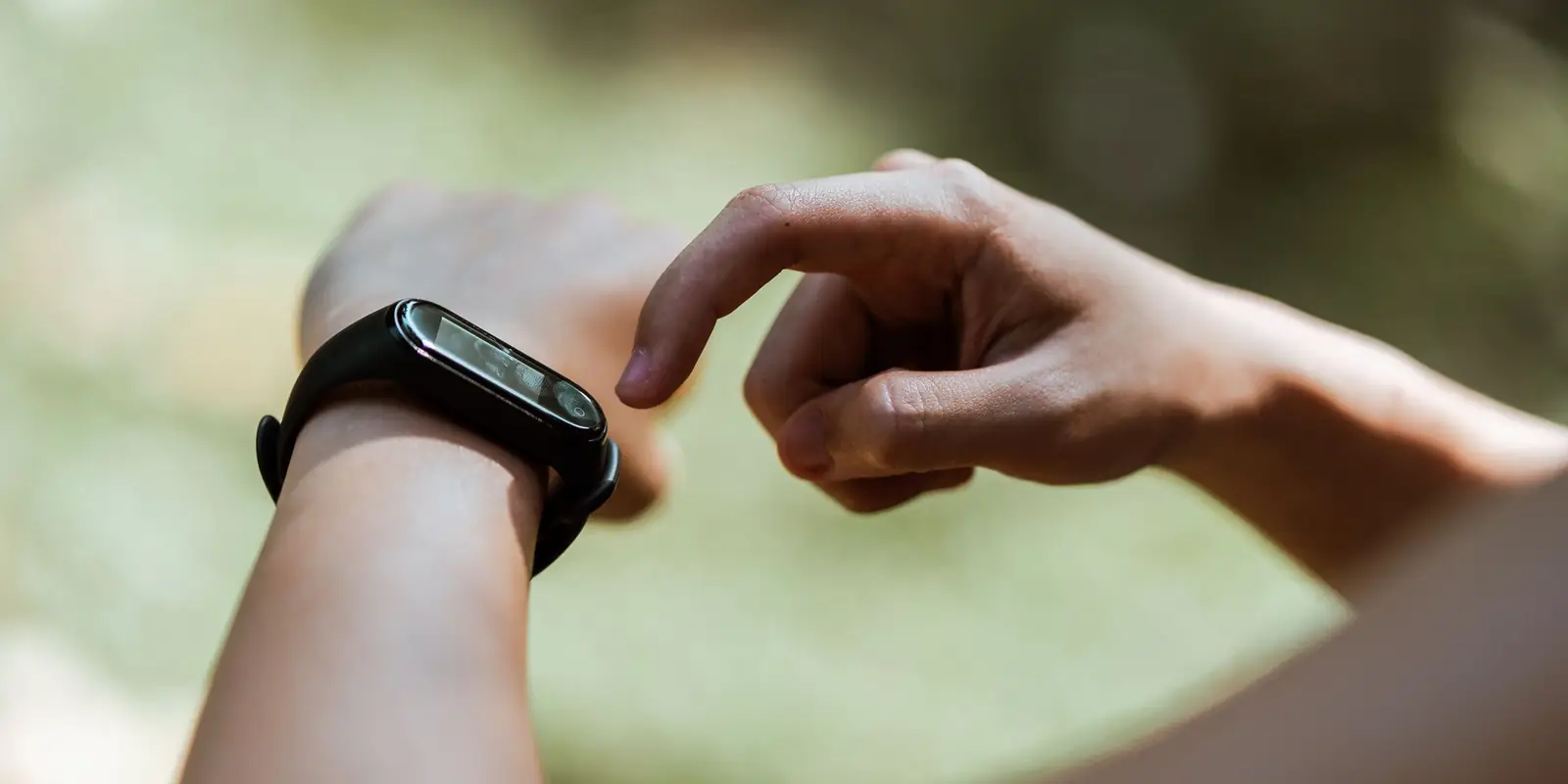 Close-up of a person tapping a slim black fitness band on their wrist outdoors