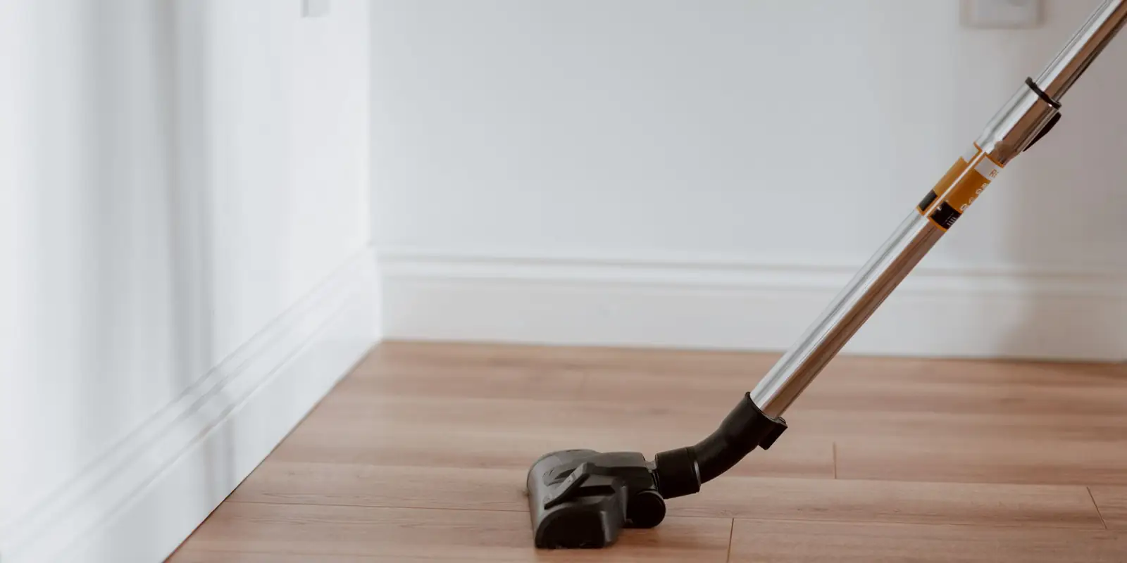Stick vacuum floor head cleaning along a skirting board on a wooden floor